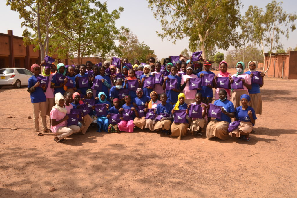 Girls holding up purple Girl Now Woman Later period kits in a our menstrual education workshop in Burkina Faso, Africa